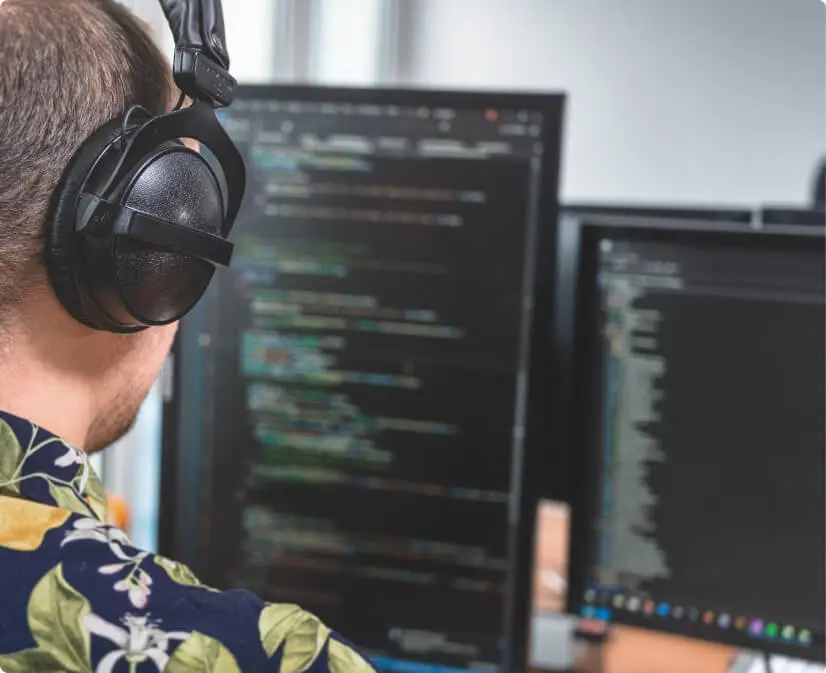 Ein Bild über die Schulter eines Mitarbeiters, der mit Kopfhörern an einem Computer arbeitet.